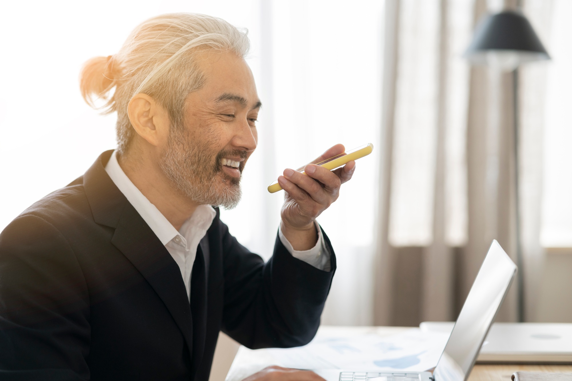 mature male japanese businessman with silver hair in office with mobile phone communication